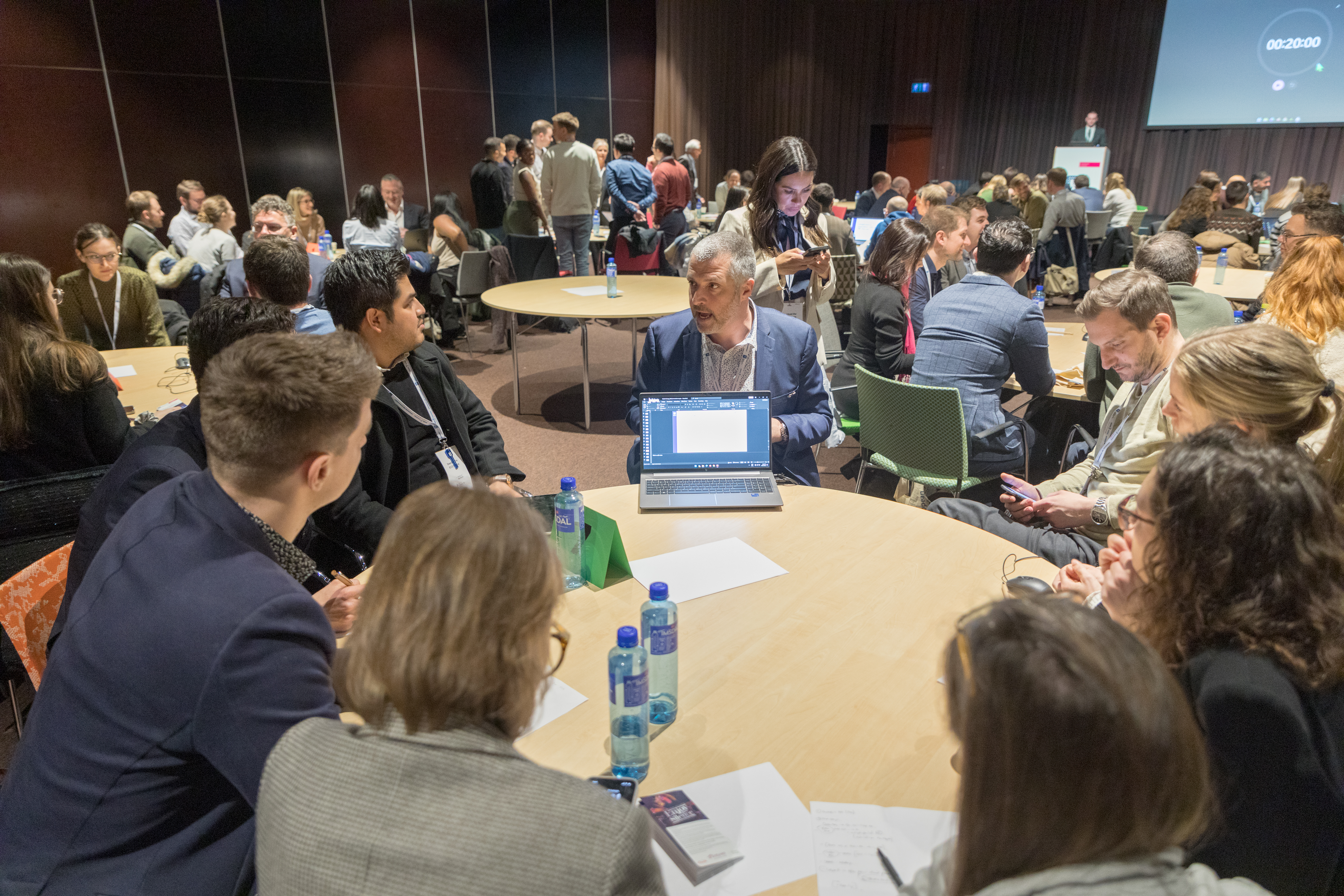 A man and a woman stand by the podium in discussion. Behind them on the screen you can see the Karolinska University Hospital and the Karolinska Institutet.