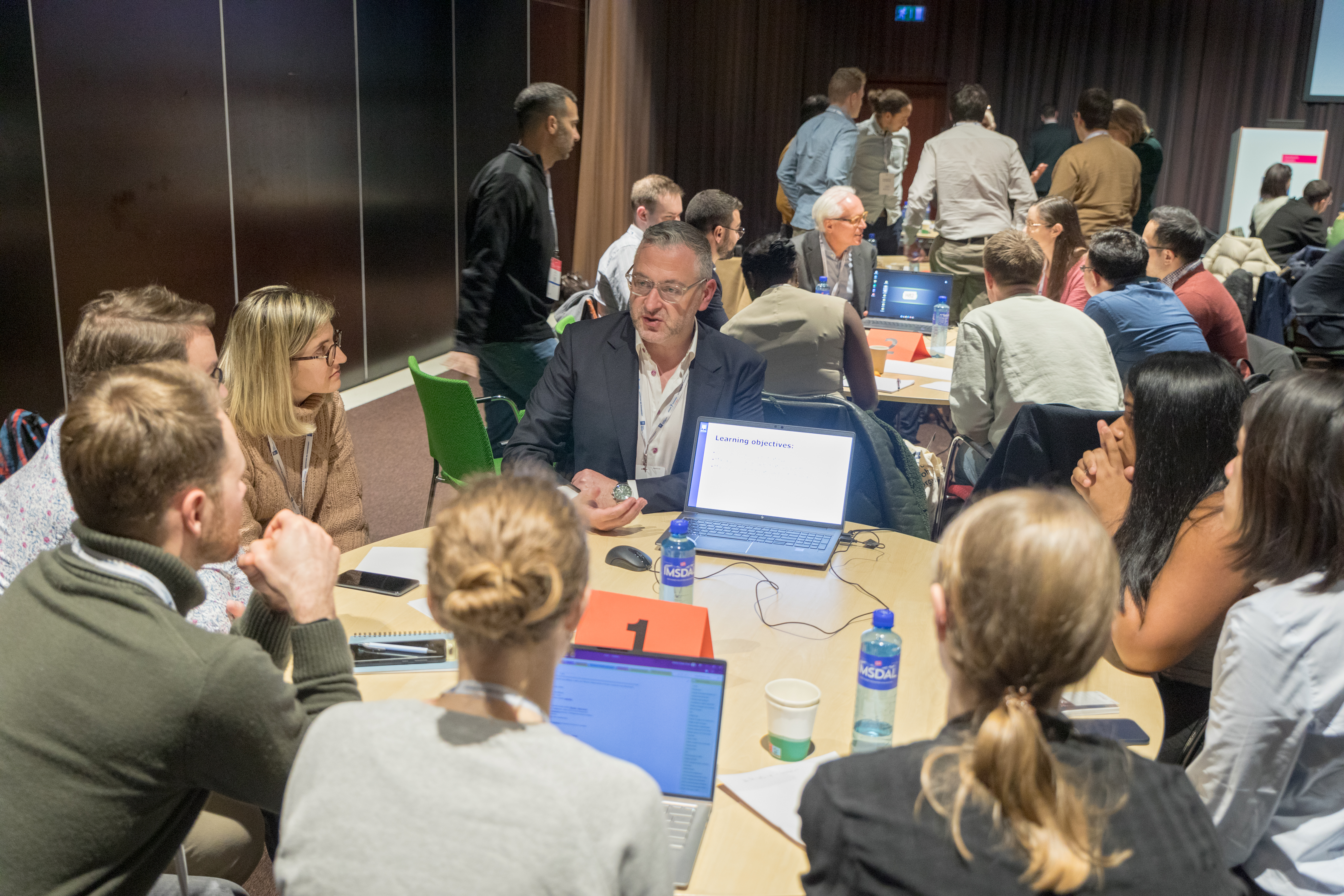Marc Ferrante and Konstantinos Papamichail sit next to the podium behind a long desk. In the background you can see the speakers conversing and the screen with a graphic of the Swedish Inflamatory Bowel Disease Registry.