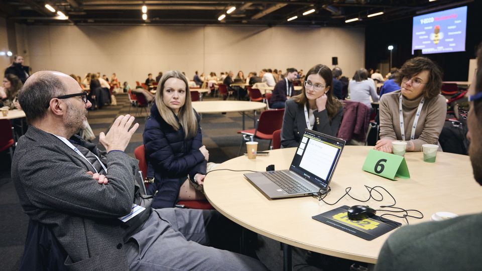 Marc Ferrante and Konstantinos Papamichail sit next to the podium behind a long desk. In the background you can see the speakers conversing and the screen with a graphic of the Swedish Inflamatory Bowel Disease Registry.