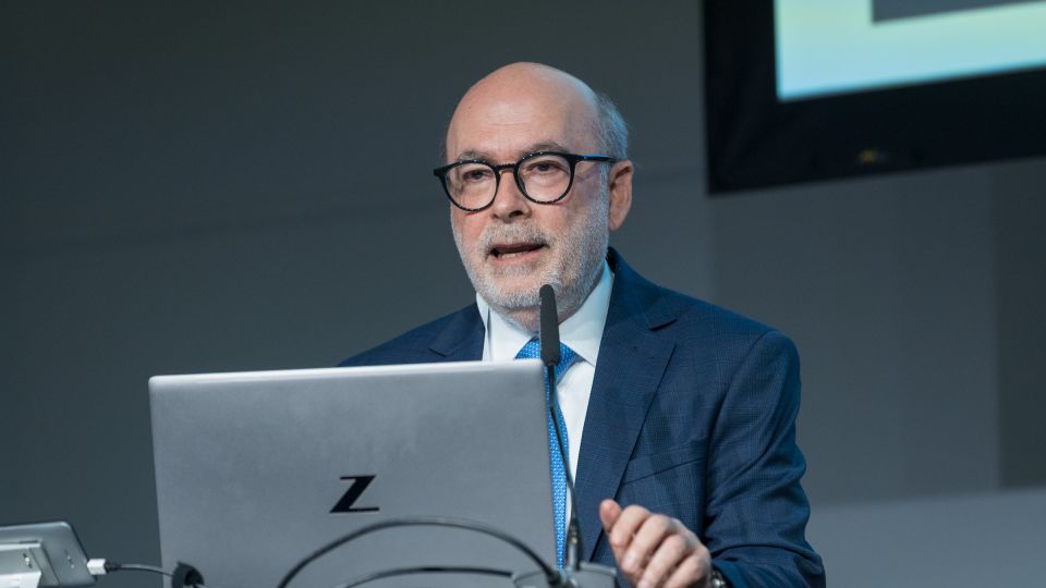 A man and a woman stand by the podium in discussion. Behind them on the screen you can see the Karolinska University Hospital and the Karolinska Institutet.