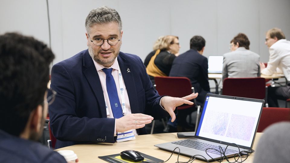 Marc Ferrante and Konstantinos Papamichail sit next to the podium behind a long desk. In the background you can see the speakers conversing and the screen with a graphic of the Swedish Inflamatory Bowel Disease Registry.