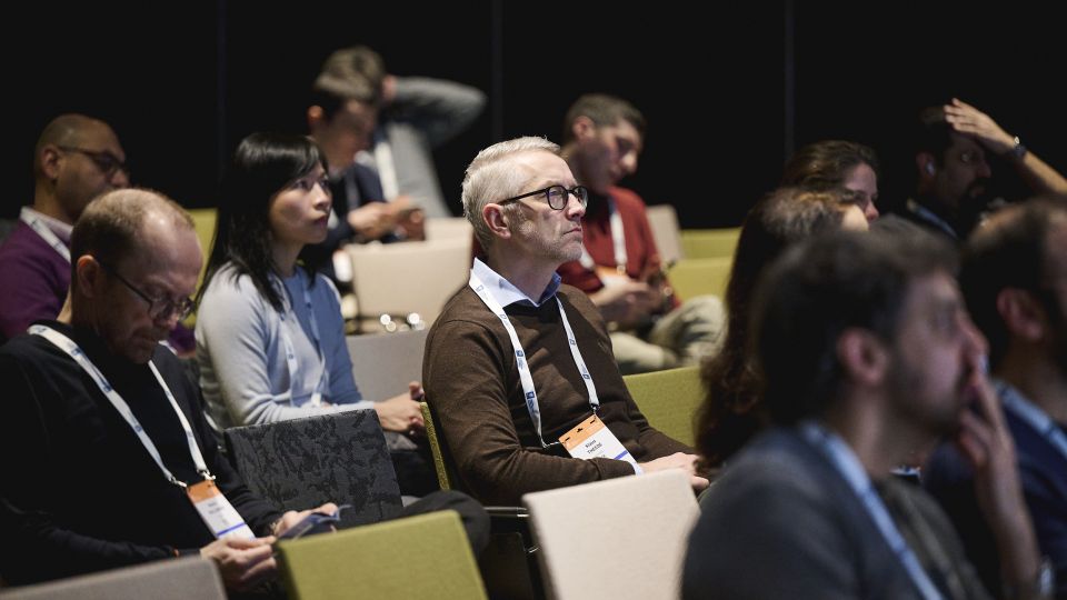 Marc Ferrante and Konstantinos Papamichail sit next to the podium behind a long desk. In the background you can see the speakers conversing and the screen with a graphic of the Swedish Inflamatory Bowel Disease Registry.