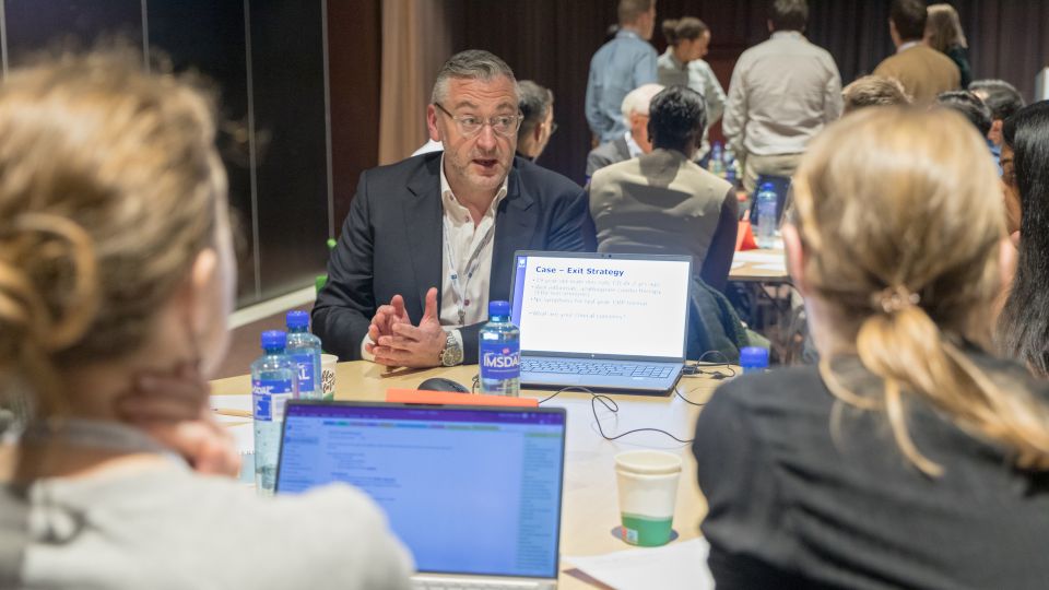 Marc Ferrante and Konstantinos Papamichail sit next to the podium behind a long desk. In the background you can see the speakers conversing and the screen with a graphic of the Swedish Inflamatory Bowel Disease Registry.