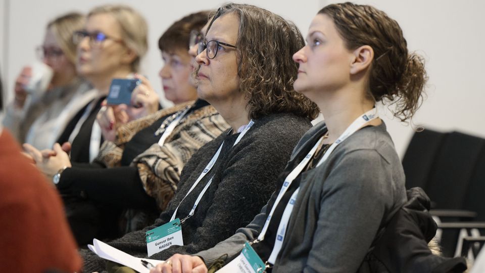 Marc Ferrante and Konstantinos Papamichail sit next to the podium behind a long desk. In the background you can see the speakers conversing and the screen with a graphic of the Swedish Inflamatory Bowel Disease Registry.
