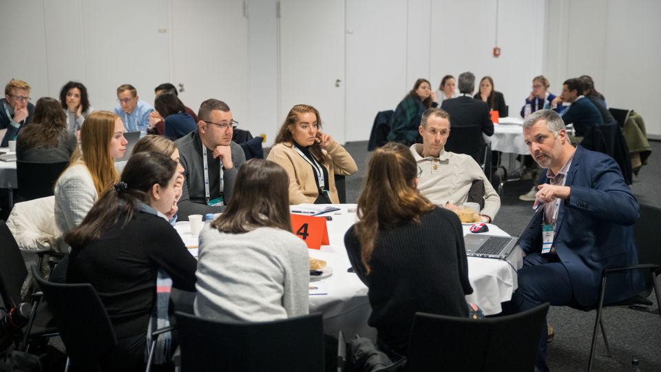 A man and a woman stand by the podium in discussion. Behind them on the screen you can see the Karolinska University Hospital and the Karolinska Institutet.