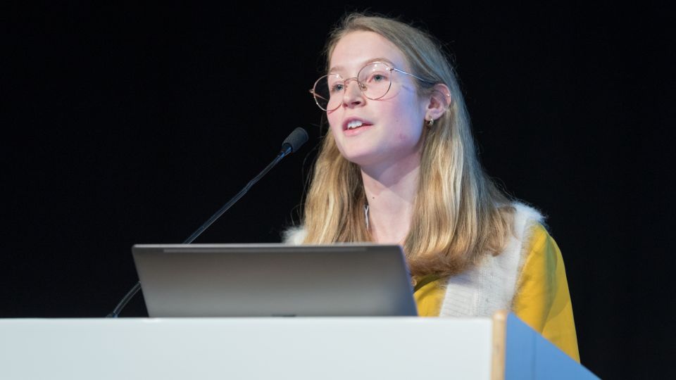 Marc Ferrante and Konstantinos Papamichail sit next to the podium behind a long desk. In the background you can see the speakers conversing and the screen with a graphic of the Swedish Inflamatory Bowel Disease Registry.