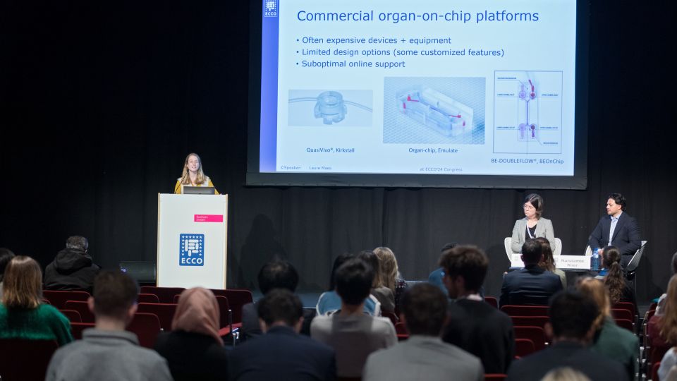 A man and a woman stand by the podium in discussion. Behind them on the screen you can see the Karolinska University Hospital and the Karolinska Institutet.