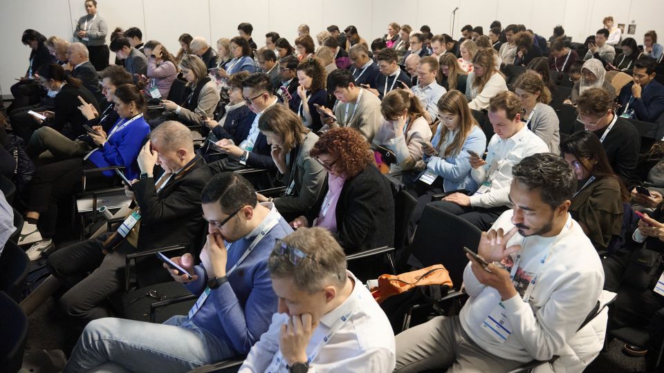 Marc Ferrante and Konstantinos Papamichail sit next to the podium behind a long desk. In the background you can see the speakers conversing and the screen with a graphic of the Swedish Inflamatory Bowel Disease Registry.