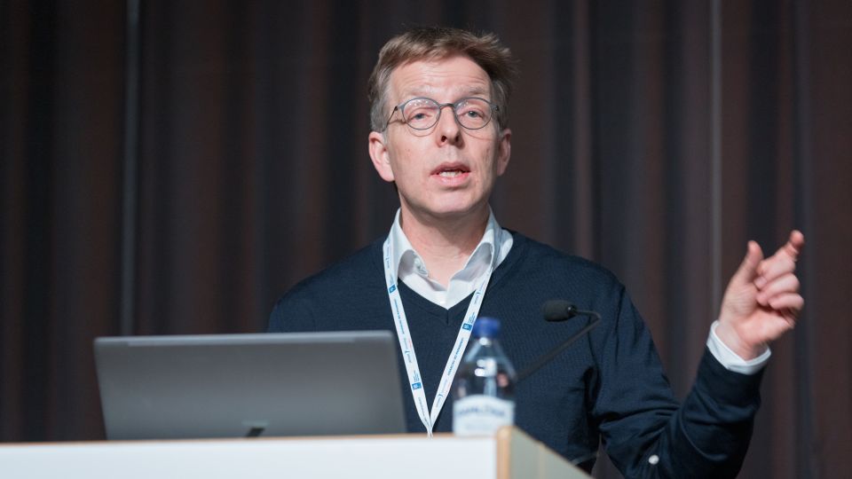 Marc Ferrante and Konstantinos Papamichail sit next to the podium behind a long desk. In the background you can see the speakers conversing and the screen with a graphic of the Swedish Inflamatory Bowel Disease Registry.