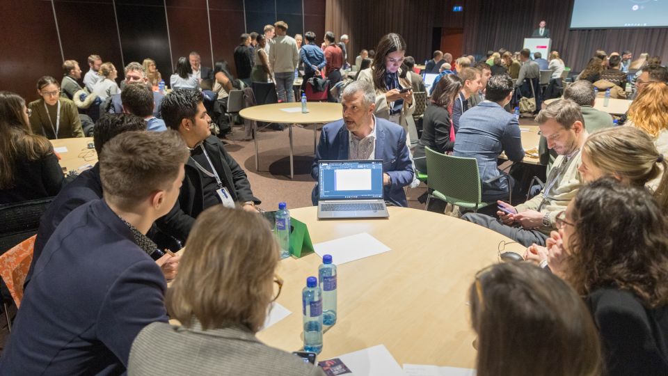 A man and a woman stand by the podium in discussion. Behind them on the screen you can see the Karolinska University Hospital and the Karolinska Institutet.