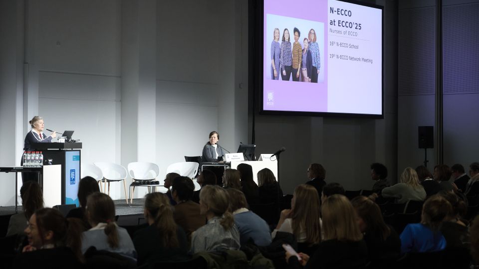 Marc Ferrante and Konstantinos Papamichail sit next to the podium behind a long desk. In the background you can see the speakers conversing and the screen with a graphic of the Swedish Inflamatory Bowel Disease Registry.
