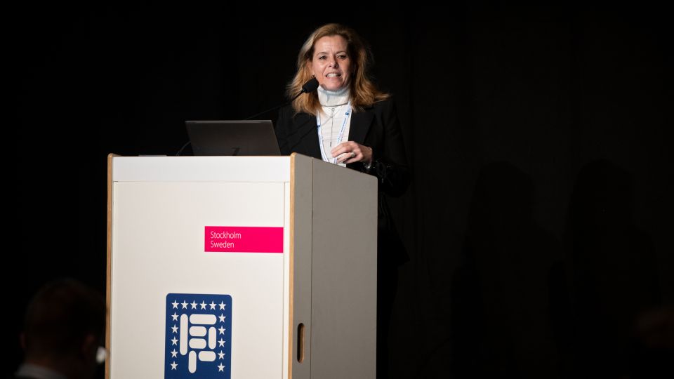 A man and a woman stand by the podium in discussion. Behind them on the screen you can see the Karolinska University Hospital and the Karolinska Institutet.