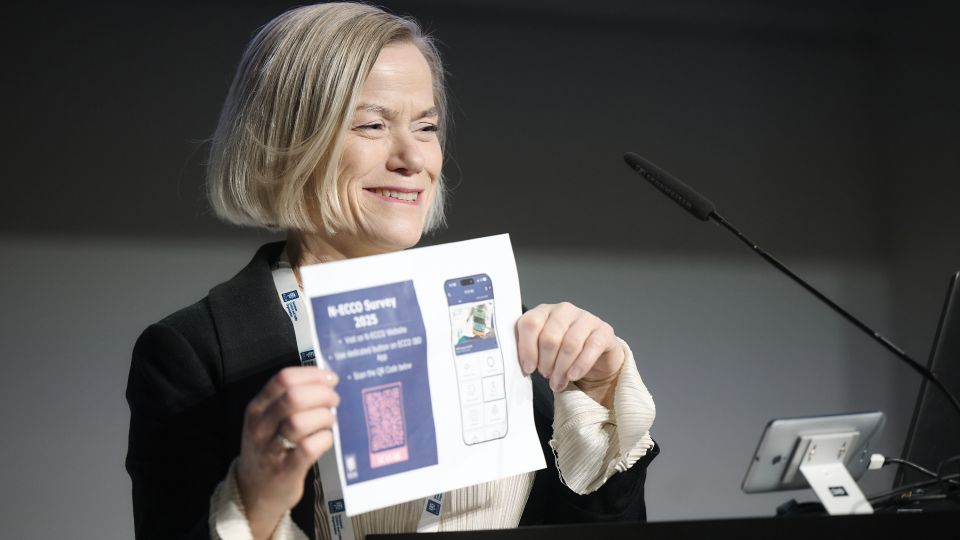 A man and a woman stand by the podium in discussion. Behind them on the screen you can see the Karolinska University Hospital and the Karolinska Institutet.