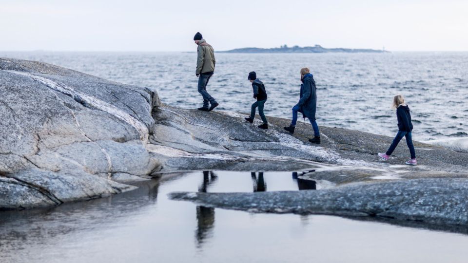 A family walks on large rocks beside the sea and an island is visibla on the horizon.