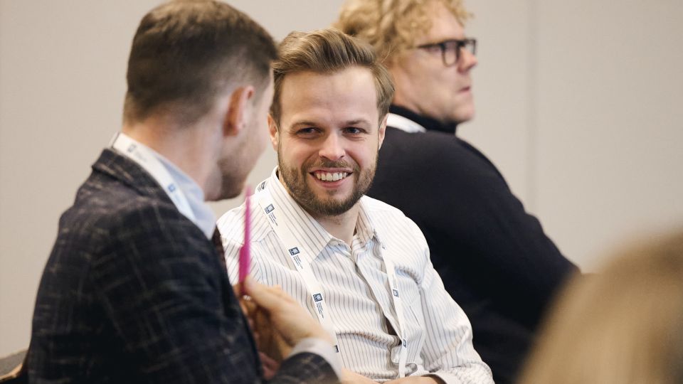 Marc Ferrante and Konstantinos Papamichail sit next to the podium behind a long desk. In the background you can see the speakers conversing and the screen with a graphic of the Swedish Inflamatory Bowel Disease Registry.