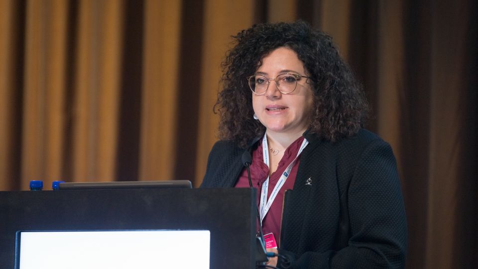 Marc Ferrante and Konstantinos Papamichail sit next to the podium behind a long desk. In the background you can see the speakers conversing and the screen with a graphic of the Swedish Inflamatory Bowel Disease Registry.