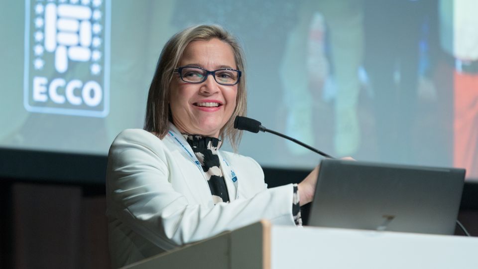 A man and a woman stand by the podium in discussion. Behind them on the screen you can see the Karolinska University Hospital and the Karolinska Institutet.