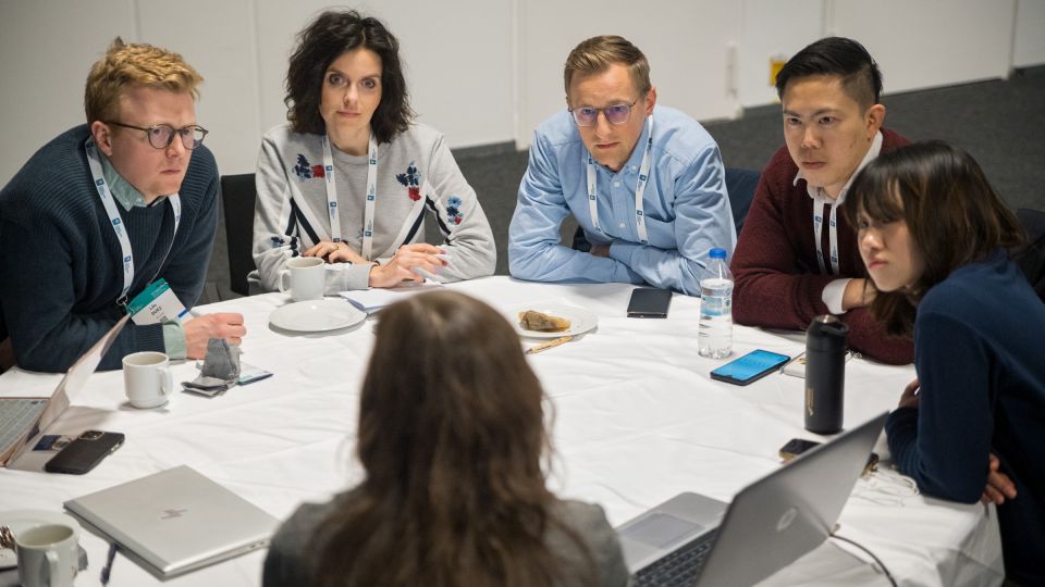Marc Ferrante and Konstantinos Papamichail sit next to the podium behind a long desk. In the background you can see the speakers conversing and the screen with a graphic of the Swedish Inflamatory Bowel Disease Registry.